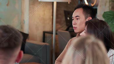 Young serious stressed 20s Asian manager businessman is anxious and bored, tired of sitting at busy office team meeting.