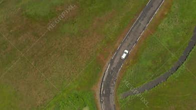 Top Down Overhead Aerial View of Electric Vehicle driving trough Nature on small road surrounded by Rich Green Grass