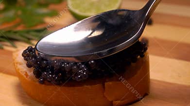 Close-up of a spoon pressing delicious black caviar to the bread slice