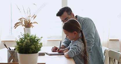 Focused primary schoolgirl studying together with caring parent.