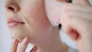 Gua Sha Massage. A young woman gives herself a gouache massage with a quartz scraper. Close-up of the cheek. White