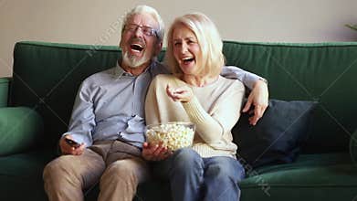 Happy old couple holding remote control laughing watching tv show