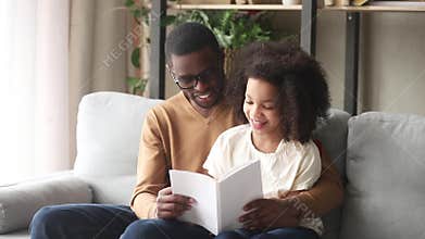 Loving black father embrace kid daughter reading book at home
