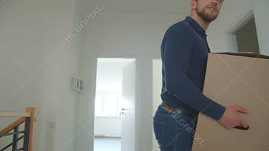Caucasian couple brings cardboard box into a new house and looking around being happy and excited.