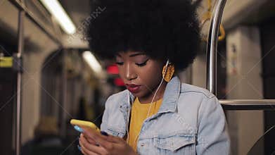 Portrait of serious african american women in headphones listening to music and browsing on mobile phone in public
