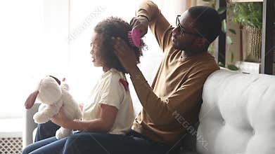 Loving black father doing brushing afro hair of kid daughter