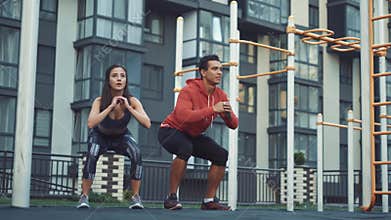 Image of young sporty man and woman 20s in tracksuits doing workout and squatting together