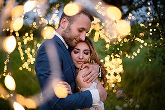 Enamored newlyweds gently embrace. Wedding ceremony in nature. The lights of the electric garland illuminate the wedding