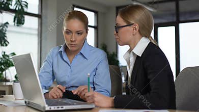 Experienced manager teaching trainee in office, explaining project on laptop