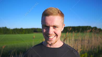 Portrait of young smiling man standing at rural environment. Handsome guy with beard looking into camera with beautiful
