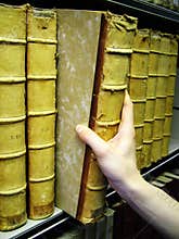 Persons hand removing old book from bookshelf