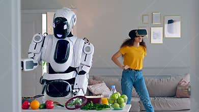 One robot cooks meal while a girl wears VR glasses.