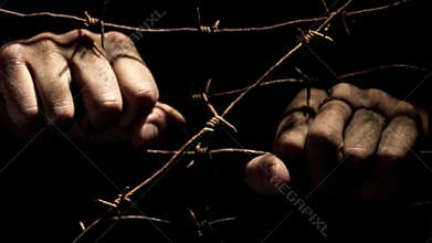 Male hands shaking rusty barbed wire in the dark lit by hard light. 4K video.