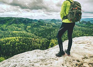 Man with a backpack and running shoes stands on top of a rock