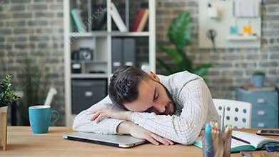 Tired businessman sleeping in workplace at desk with head on laptop computer