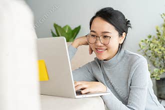 Asian woman is working on a laptop in home . On her face are smile when she work at sofa