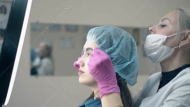 Woman holds brow ruler at client face to check tattoo