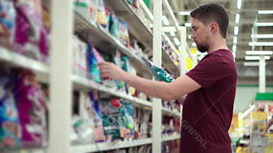 Man is reading inscriptions on pack of pet food in supermarket