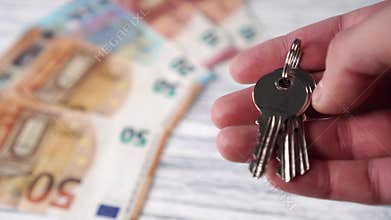 New shiny house keys on a background of heaps of euro banknotes on a white wooden table