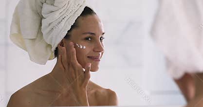 Smiling young woman apply facial creme look in mirror
