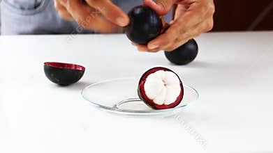 Hand peeling mangosteen fruit with knife on white table