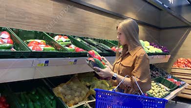 Young woman with shopping basket selecting fresh vegetables in a grocery store