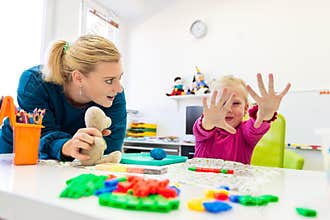 Toddler girl in child occupational therapy session doing sensory playful exercises with her therapist.