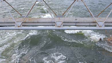 Flooding in the city, fast river current under the bridge with piping.