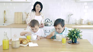 Happy family mom and two sons having breakfast in the kitchen.
