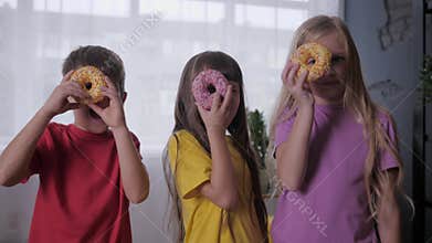 Happy childhood, carefree children look with one eye through donut during joint celebration, kids party