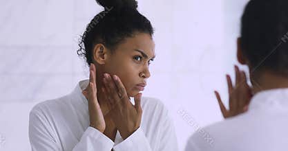 Worried african lady upset with dry skin looking in mirror