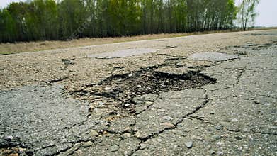A large pit on the road. Cracked ruined asphalt pit roads, panning shot in sunny summer day.