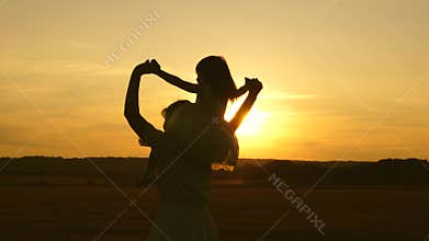 Mother carries a little daughter on her shoulders in the sun and walks in the park. Happy young family with a child in a