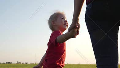 A young mother walks with her blonde daughter in the fresh air. Happy family walking on green grass.