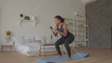 African american woman with phone squats at home