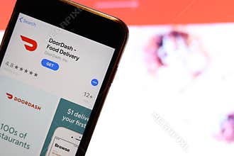 Mobile phone screen with DoorDash Food Delivery logo on app store close up with website on laptop. Blurred background