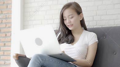 Beautiful portrait asian woman working online laptop computer with smile and happy sitting on couch