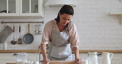 Smiling attractive 30s housewife using rolling pin.
