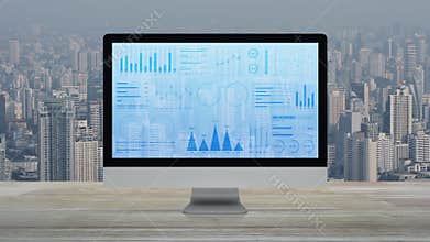 Statistics graphs, charts and diagrams data on modern computer monitor screen on wooden table over office building tower and skysc