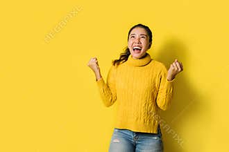 Portrait of a happy Asian woman screaming an excited and celebrating success isolated over yellow background. Succeed