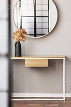 Round mirror in wooden frame above fancy console table with flowers in vase in trendy bedroom interior with beige vase