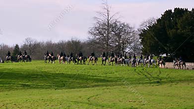 Panning shot of a line of horse riding fox hunters as they ride through Capability Brown designed parkland