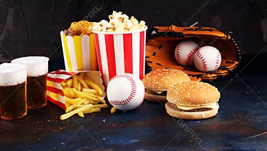 Popcorn and burger, fries and chicken nuggets on the table with draft beer. Baseball party food with balls for the playoffs