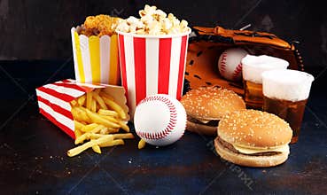 Popcorn and burger, fries and chicken nuggets on the table with draft beer. Baseball party food with balls for the playoffs