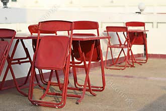 Foldable red table and chair set placed outdoors. Foldable chairs, leaning on the table.