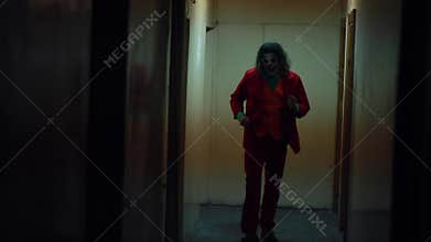 Cosplayer in the image of a crazy clown from the thriller `Joker` walks and dances in corridor.
