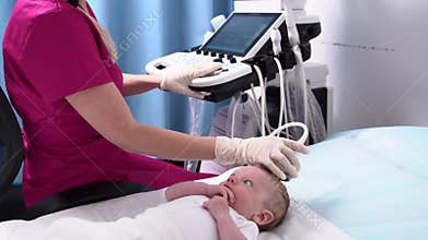 A female doctor conducts an ultrasound examination of the head and brain of a newborn baby using modern medical
