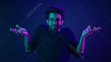 Male portrait in blue neon ultraviolet background Indian man shrug shoulders don't know gesture Arabian male guy