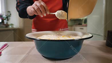 The hostess is preparing dough in the kitchen. Mixes beaten eggs with flour. Women's hands stir the mixture for