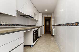 elongated kitchen with furniture on one side of the room, wooden countertop, white tiles with borders and cream-colored stoneware